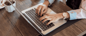 une photo d'une femme qui écrit sur son ordinateur avec un manteau rose