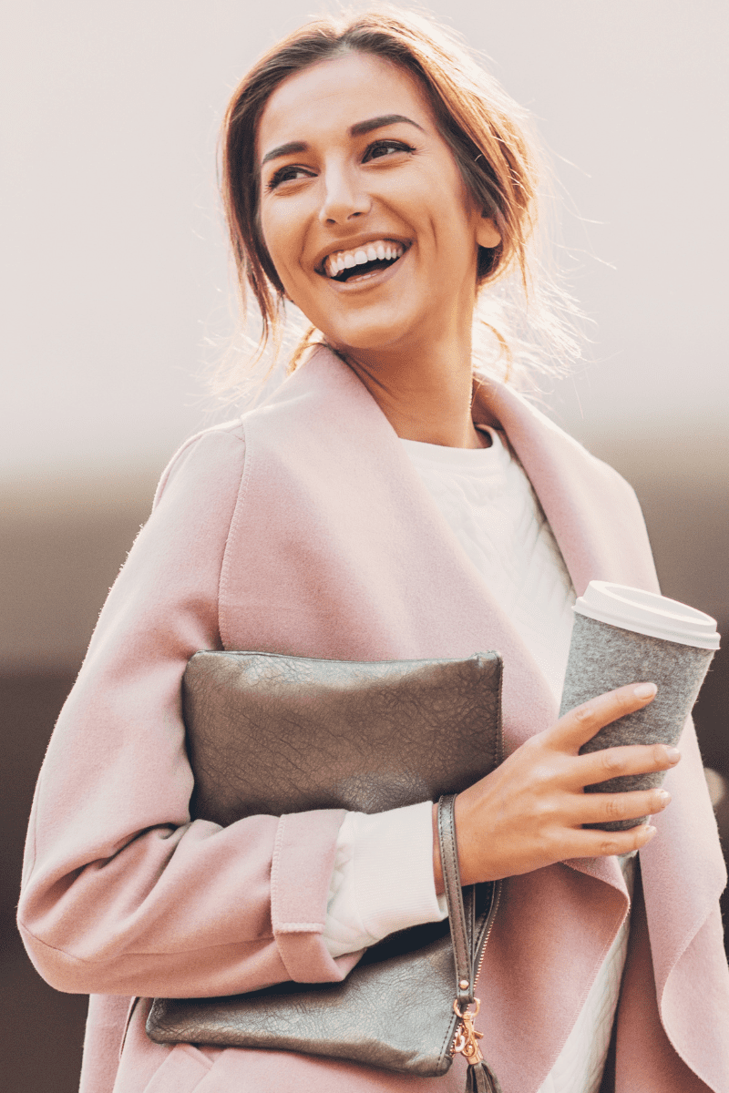 une belle femme avec un manteau rose qui sourit et bois un café.