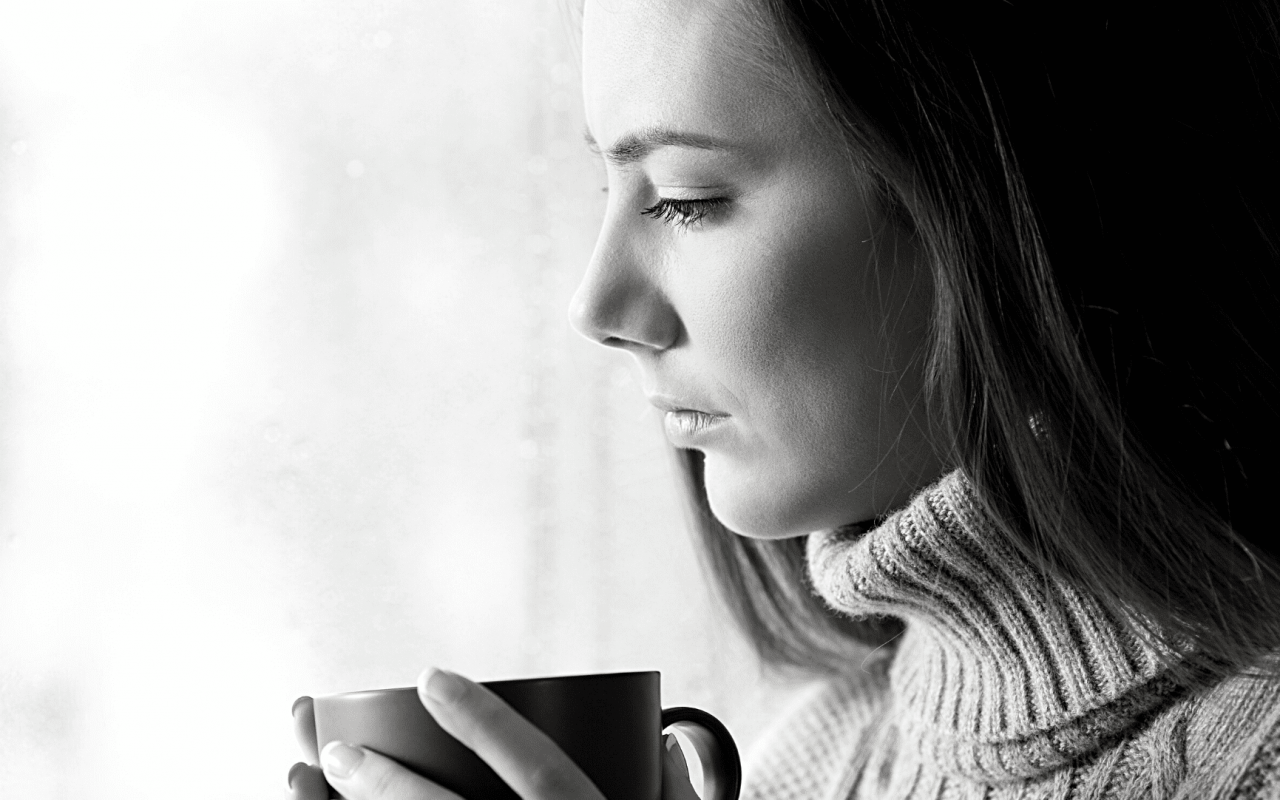une femme qui tient son café et regarde par la fenêtre